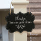 Black laminate scalloped edge sign with white lettering stating Please remove your shoes with leaf design and border hanging on stair banister