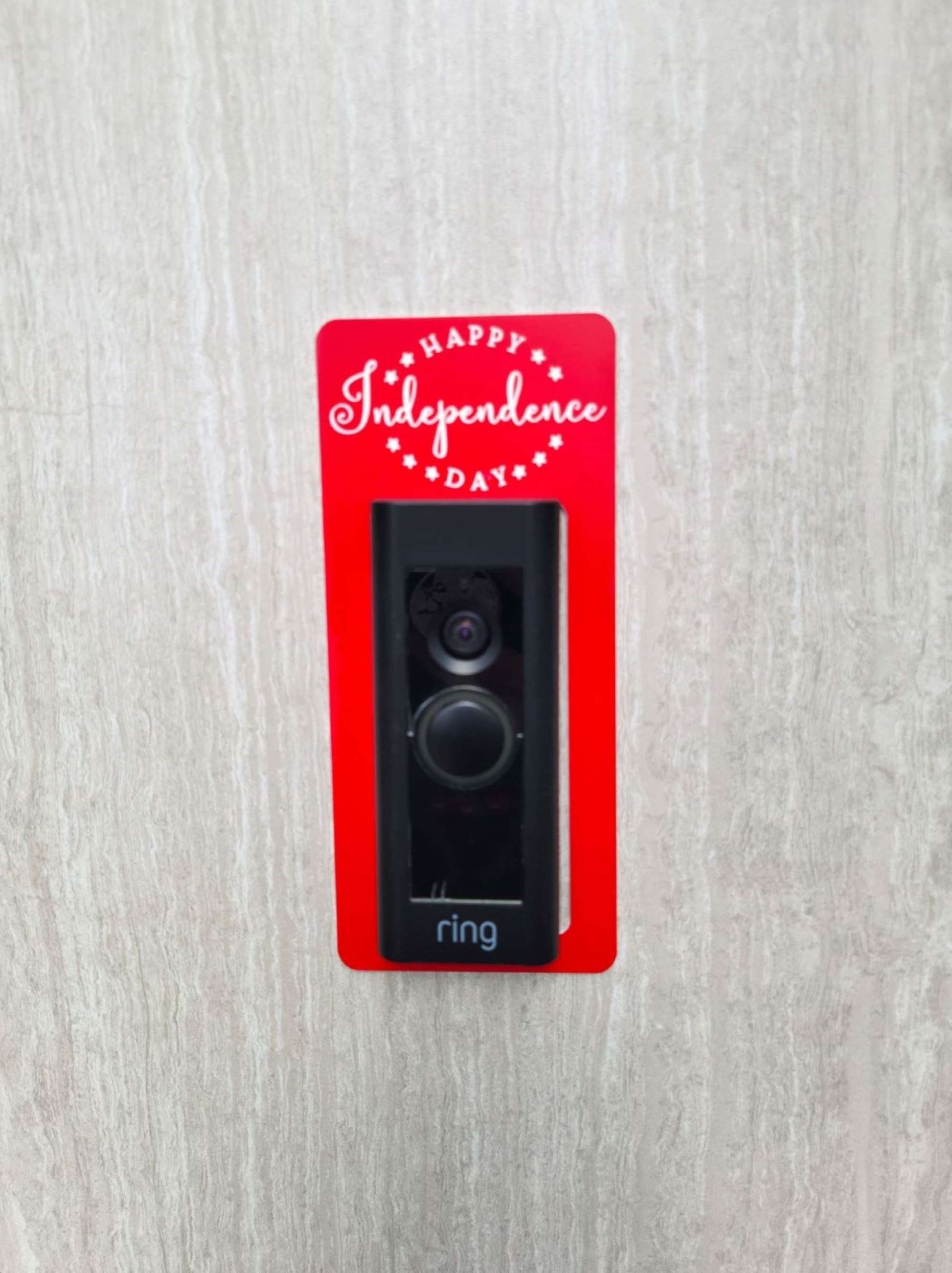 Red laminate doorbell surround with white lettering saying Happy Independence Day and stars on ring doorbell and gray background