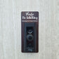 Wood grain laminate rectangle that fits around a Ring doorbell with white laser engraved lettering stating Please No Soliciting Seriously Don't Make It Weird on a neutral background