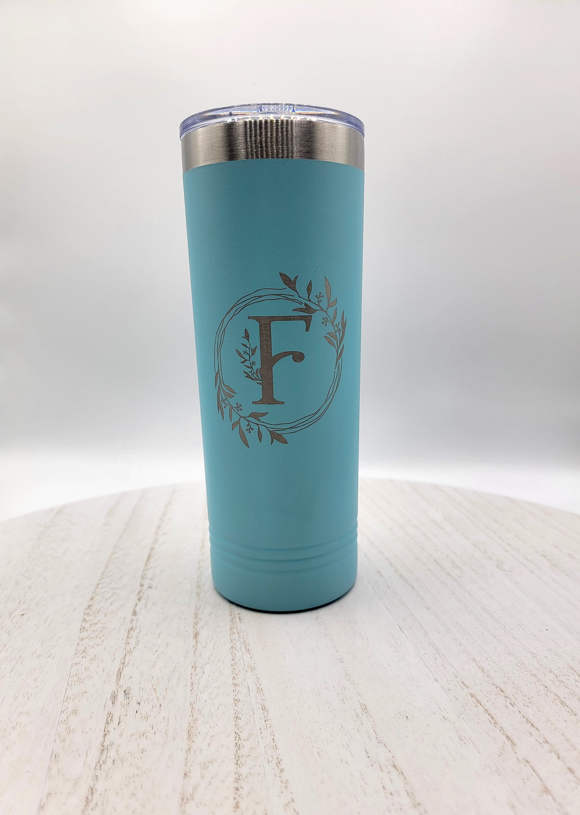 Teal skinny tumbler with floral wreath and letter F in silver on white background
