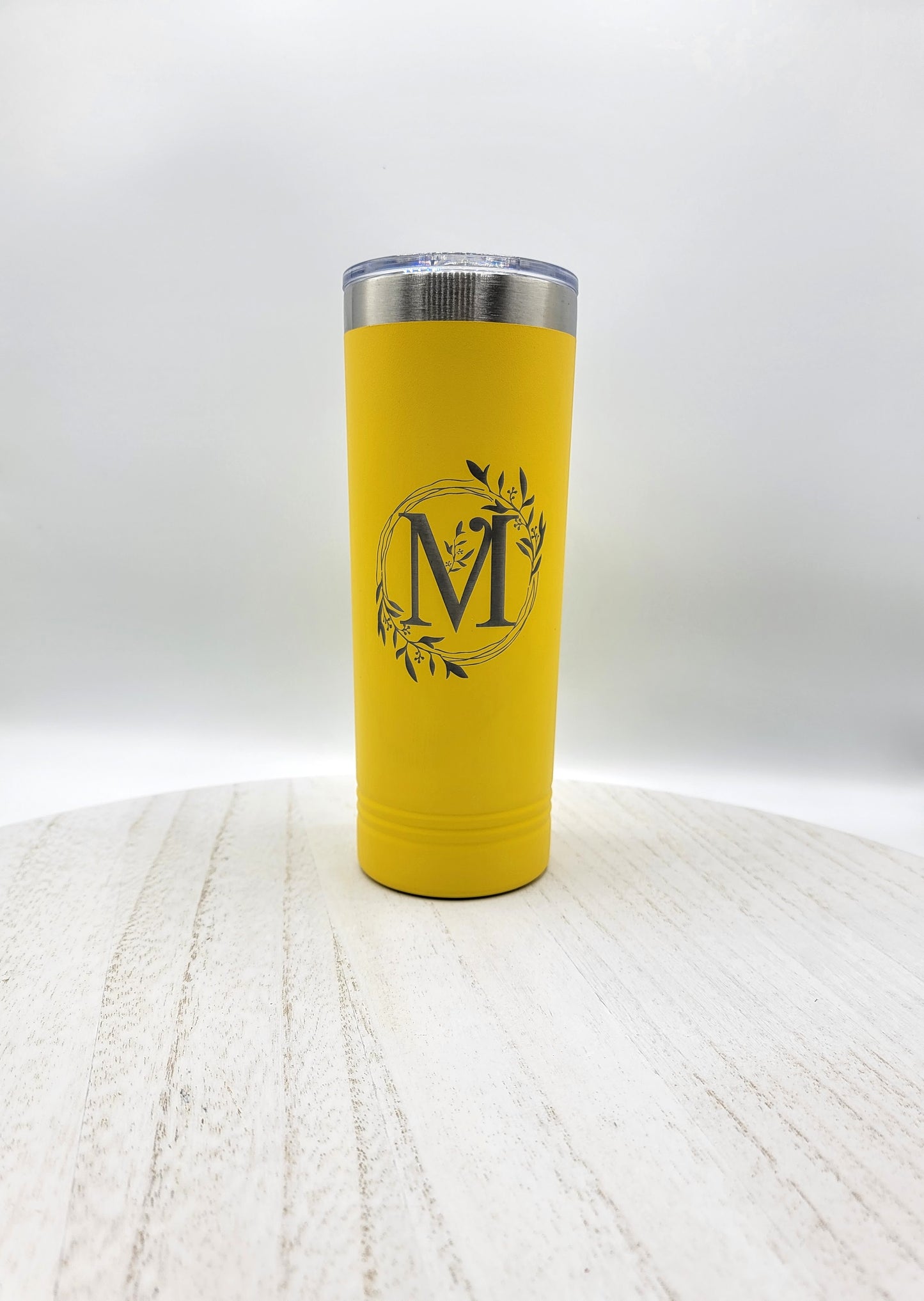 Yellow skinny tumbler with floral wreath and letter M in silver on white background