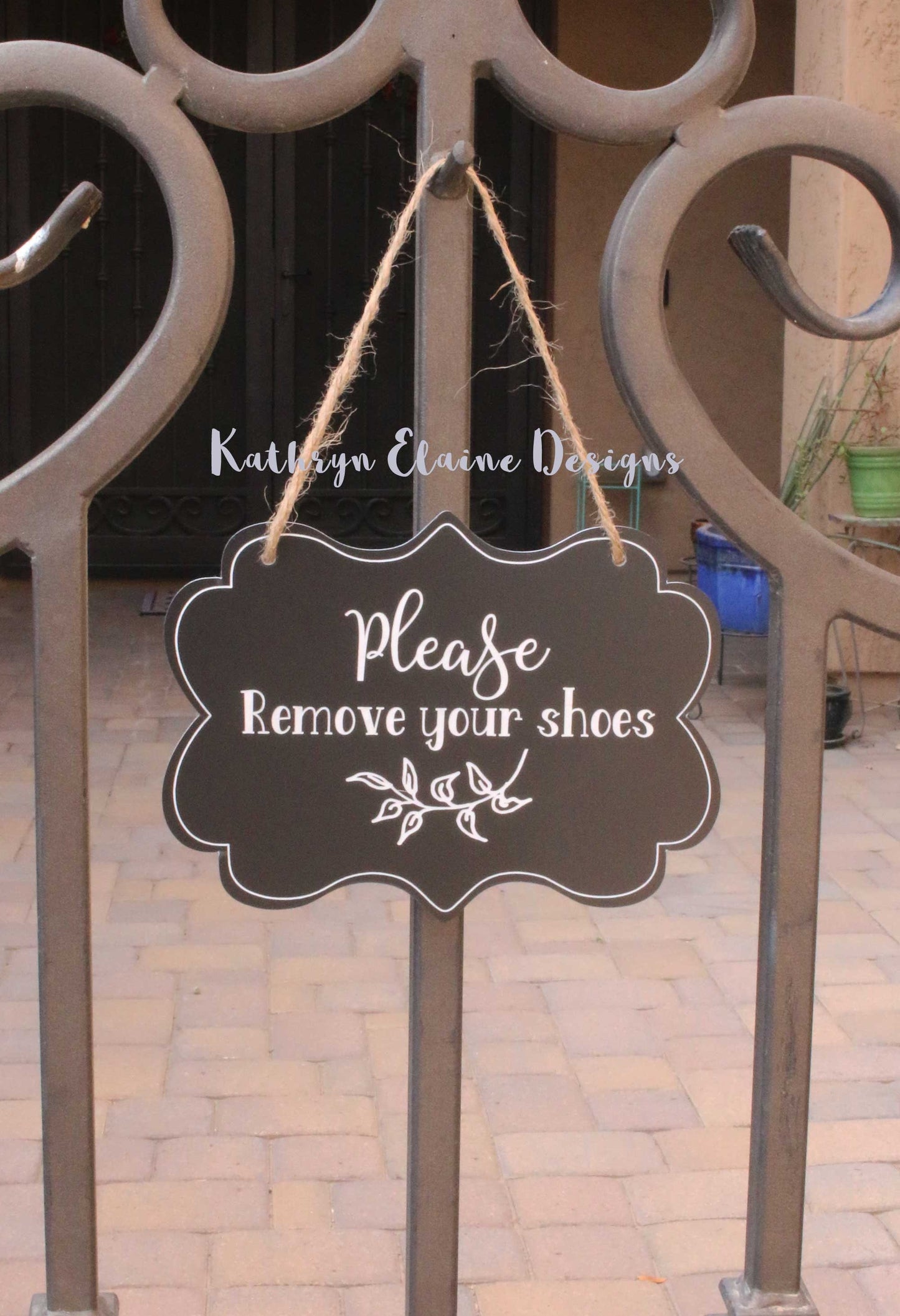 Black laminate scalloped edge sign with white lettering stating Please remove your shoes with leaf design and border on outdoor gate
