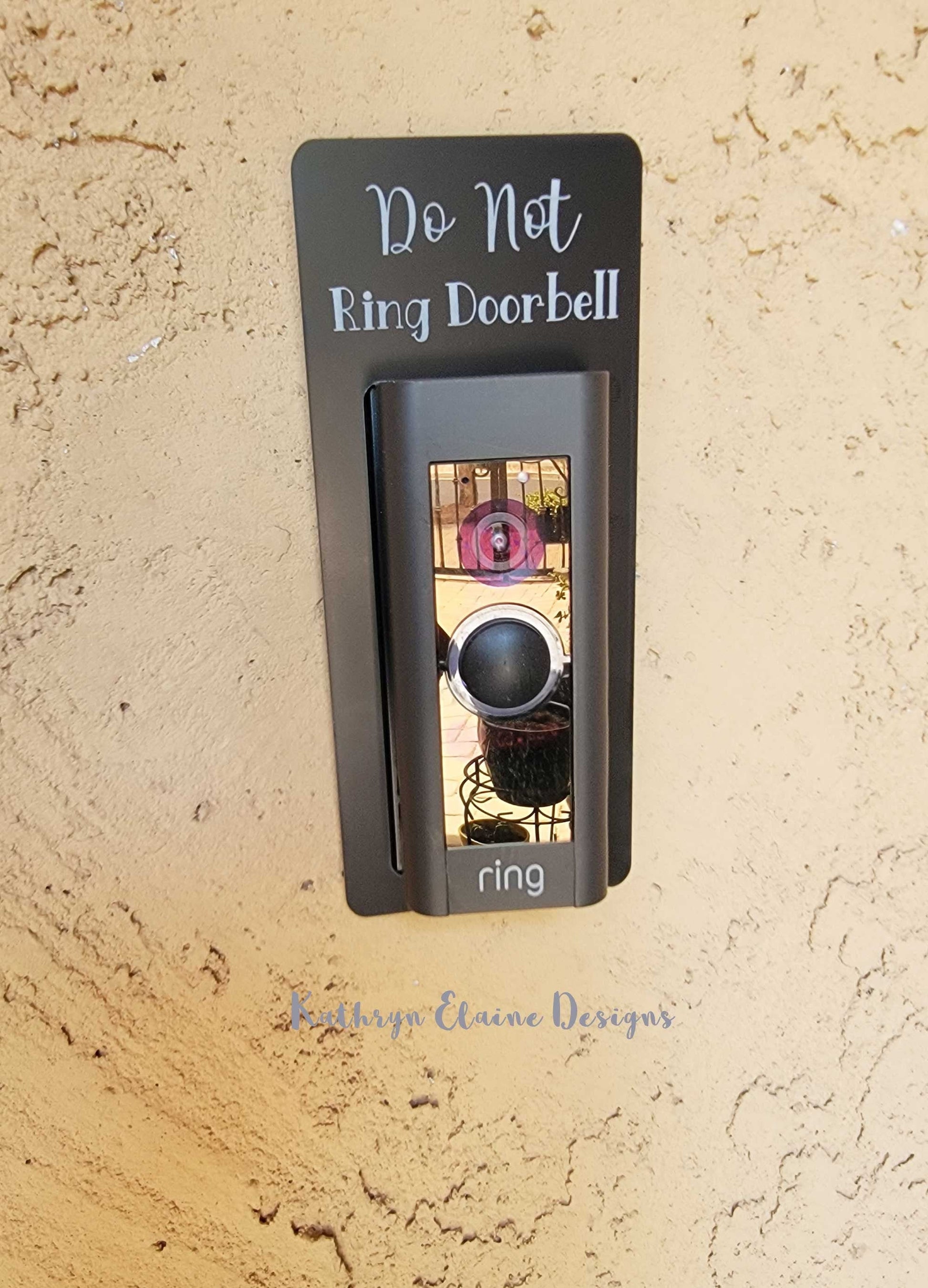 Black laminate doorbell surround with white lettering stating Do Not Ring Doorbell on Ring doorbell and tan background