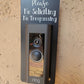 Black laminate rectangle that fits around a Ring doorbell with white laser engraved lettering stating Please No Soliciting No Trespassing on a tan background