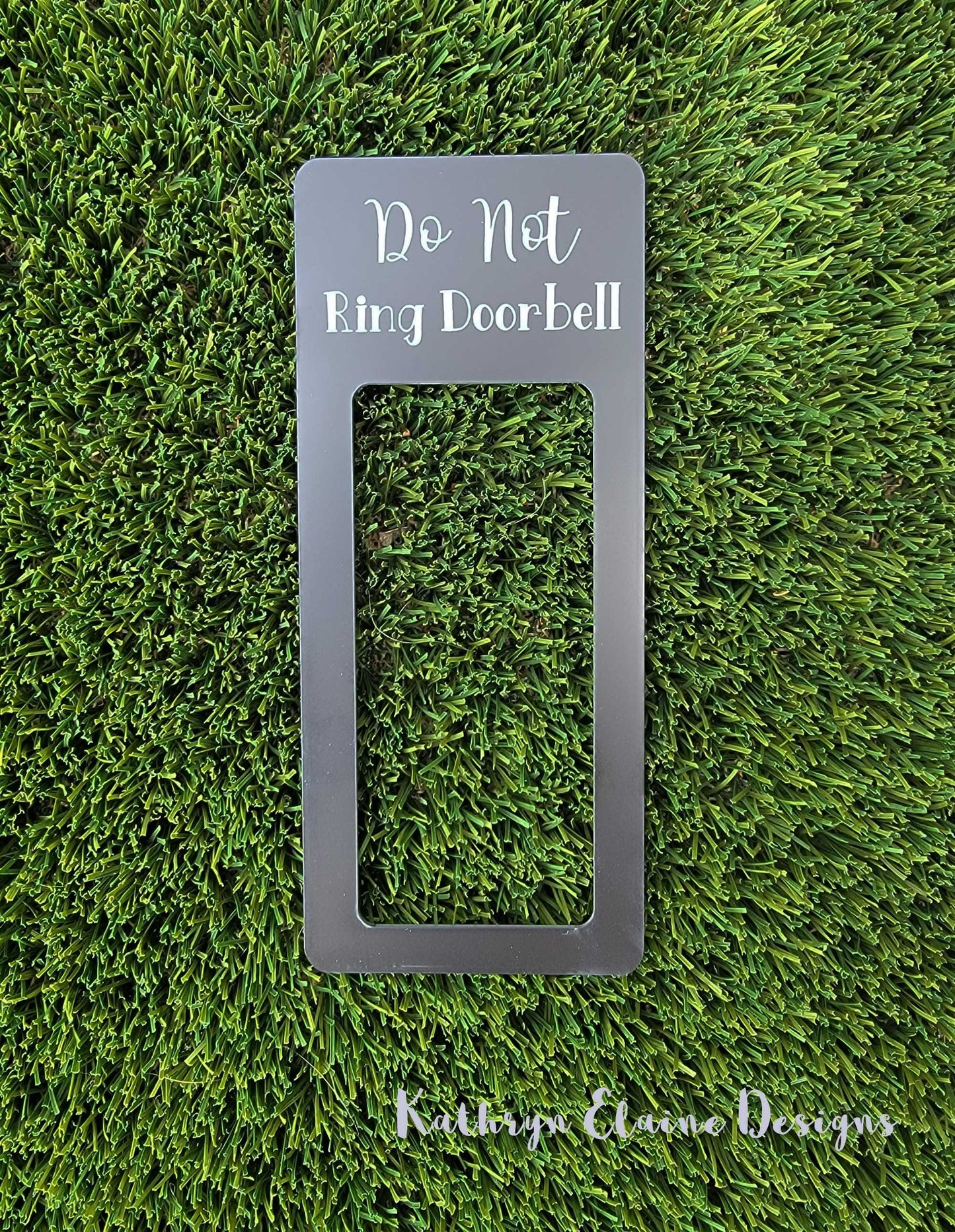 Black laminate doorbell surround with white lettering stating Do Not Ring Doorbell on grass background