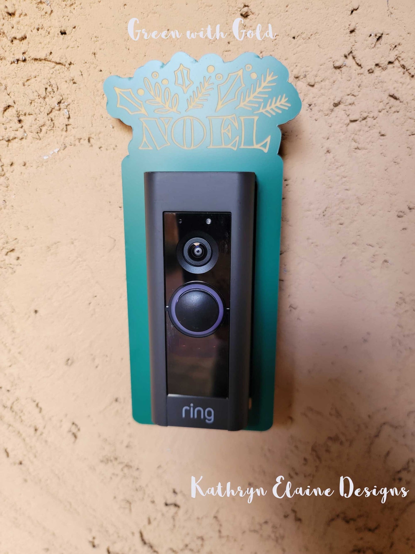Green laminate doorbell surround with golden lettering saying Noel and holly, leaf design around ring doorbell on tan background.