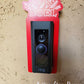 Red laminate doorbell surround with white lettering saying Noel and holly, leaf design around ring doorbell on tan background.
