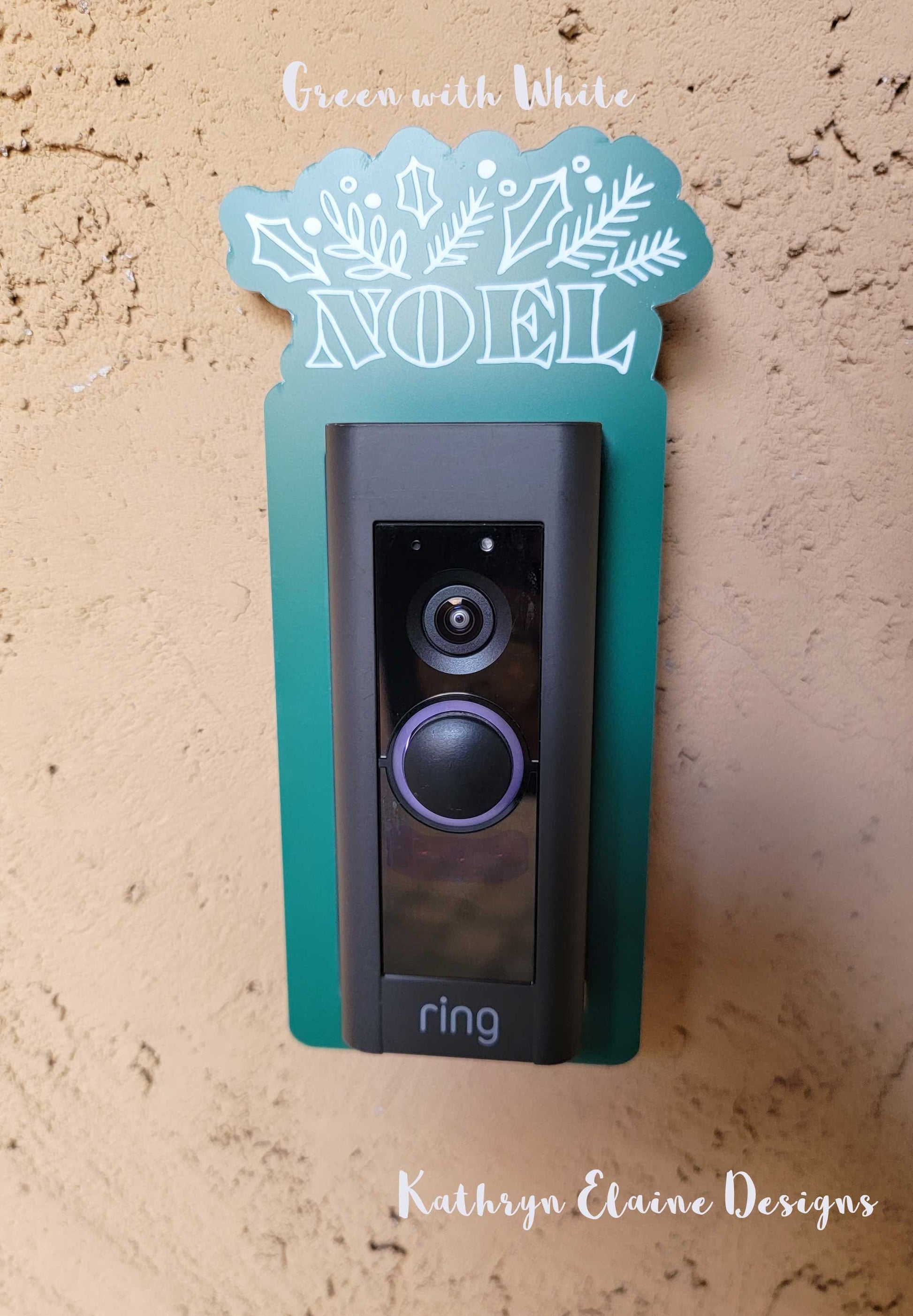 Green laminate doorbell surround with white lettering saying Noel and holly, leaf design around ring doorbell on tan background.