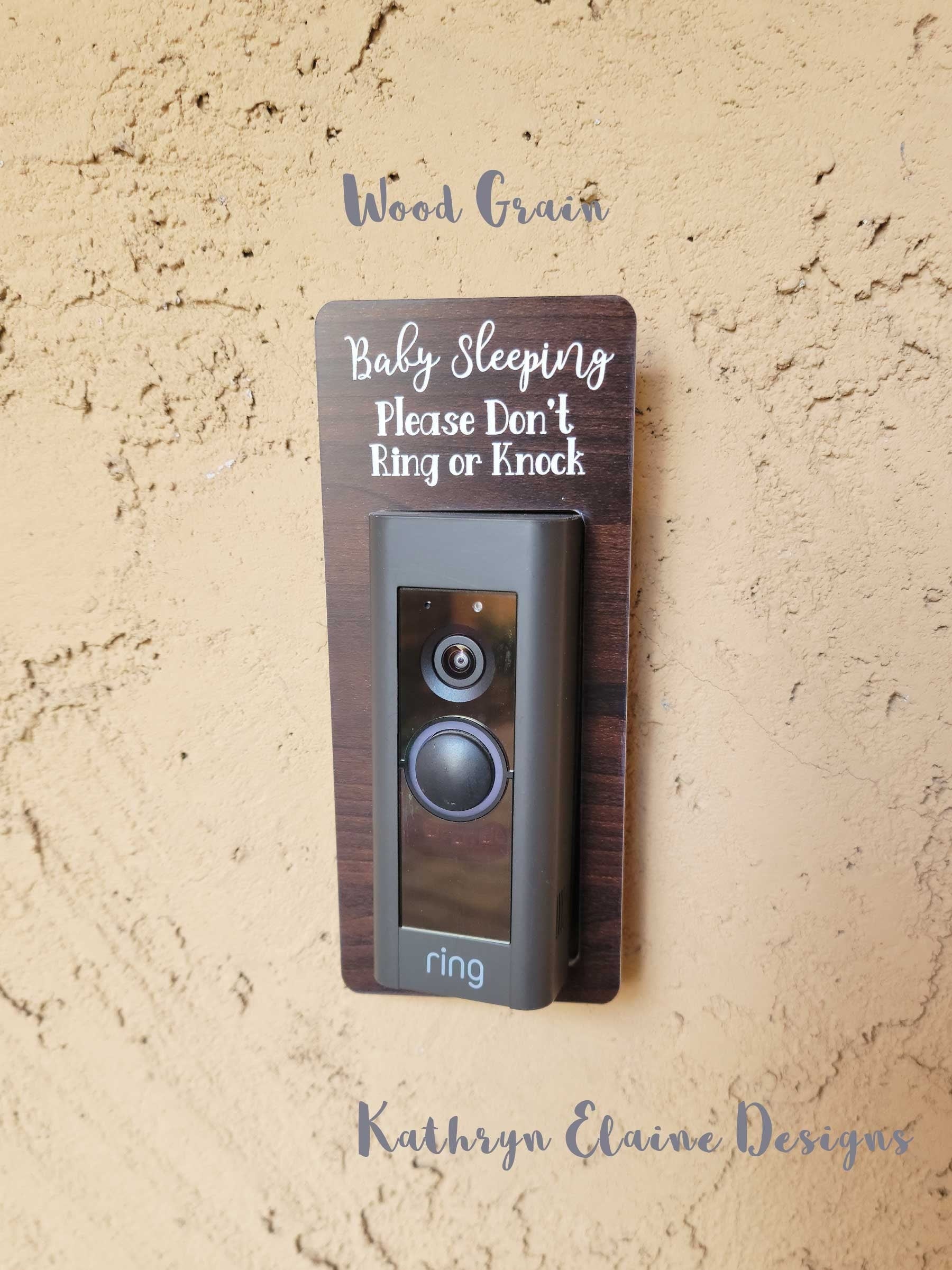 Wood grain laminate rectangle around Ring doorbell that says Baby Sleeping Please Don't Ring or Knock in white lettering against tan stucco background