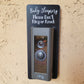 Black laminate rectangle around Ring doorbell that says Baby Sleeping Please Don't Ring or Knock in white lettering against tan stucco background