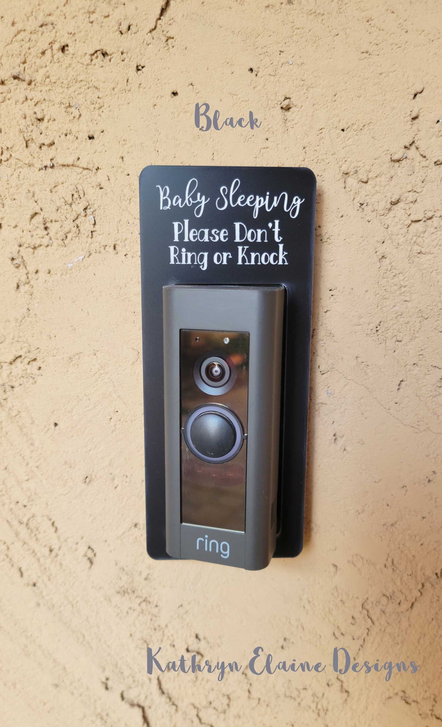 Black laminate rectangle around Ring doorbell that says Baby Sleeping Please Don't Ring or Knock in white lettering against tan stucco background