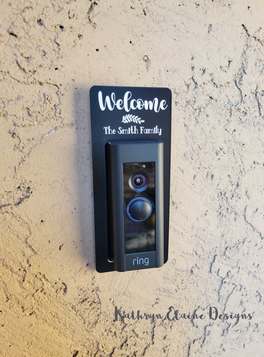 Black laminate doorbell surround stating Welcome (leaf design) the Smith Family in white writing around Ring doorbell on tan background.