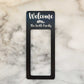 Black laminate doorbell surround stating Welcome (leaf design) the Smith Family in white writing on marble background.