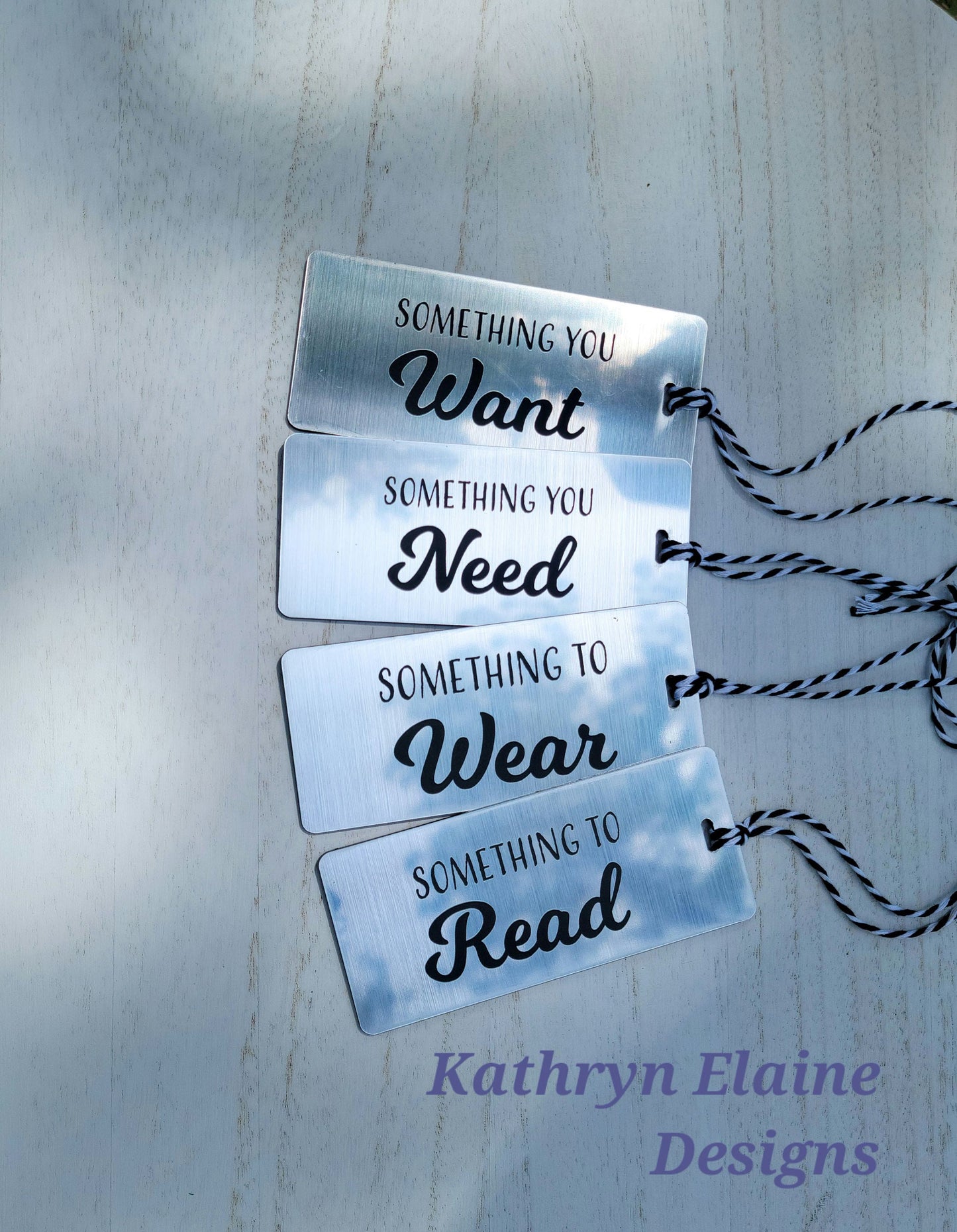 4 gift tags in silver with black lettering reading something you want, something you need, something to wear, something to read on white background