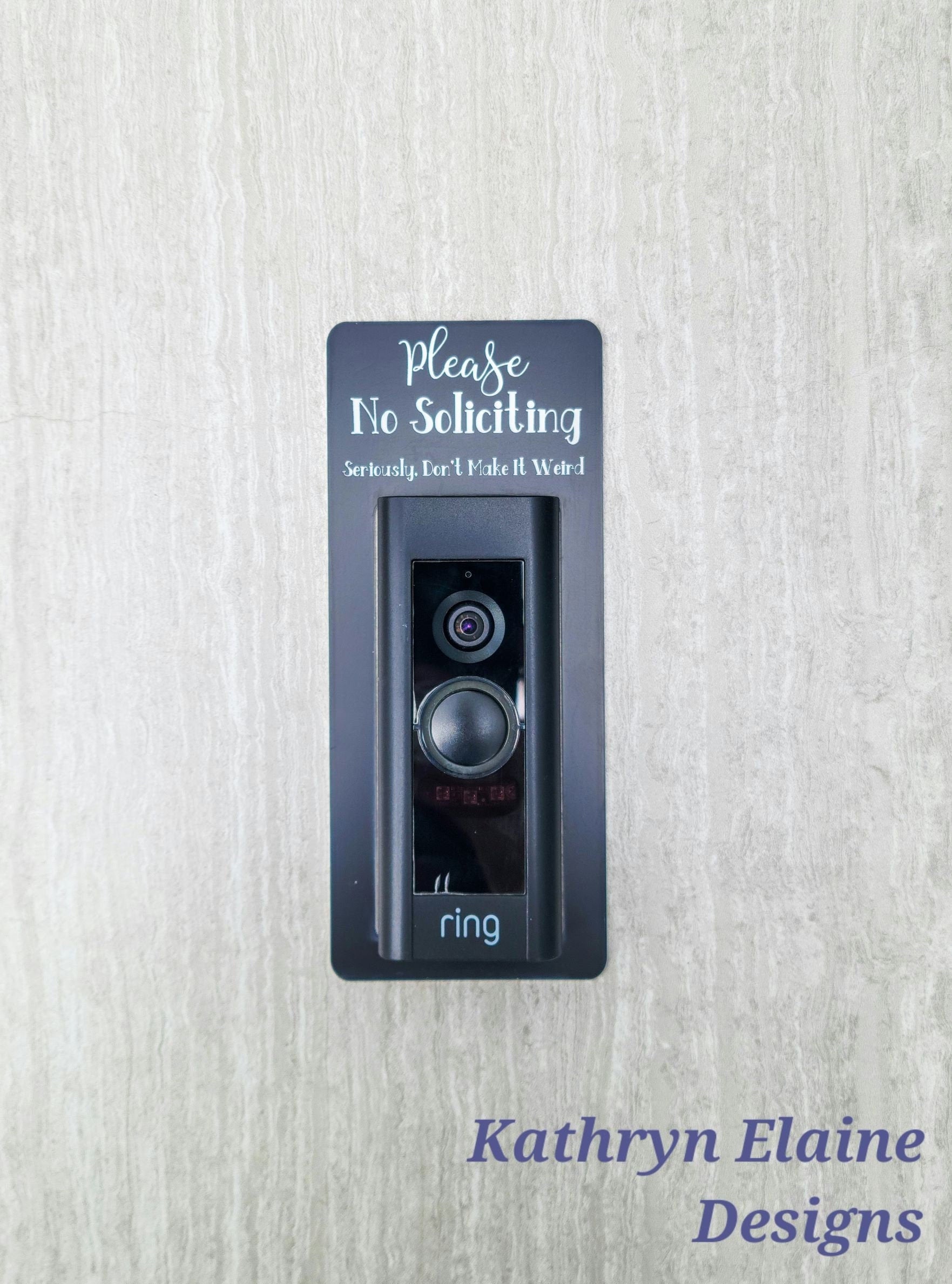 Black laminate rectangle that fits around a Ring doorbell with white laser engraved lettering stating Please No Soliciting Seriously Don't Make It Weird on a neutral background