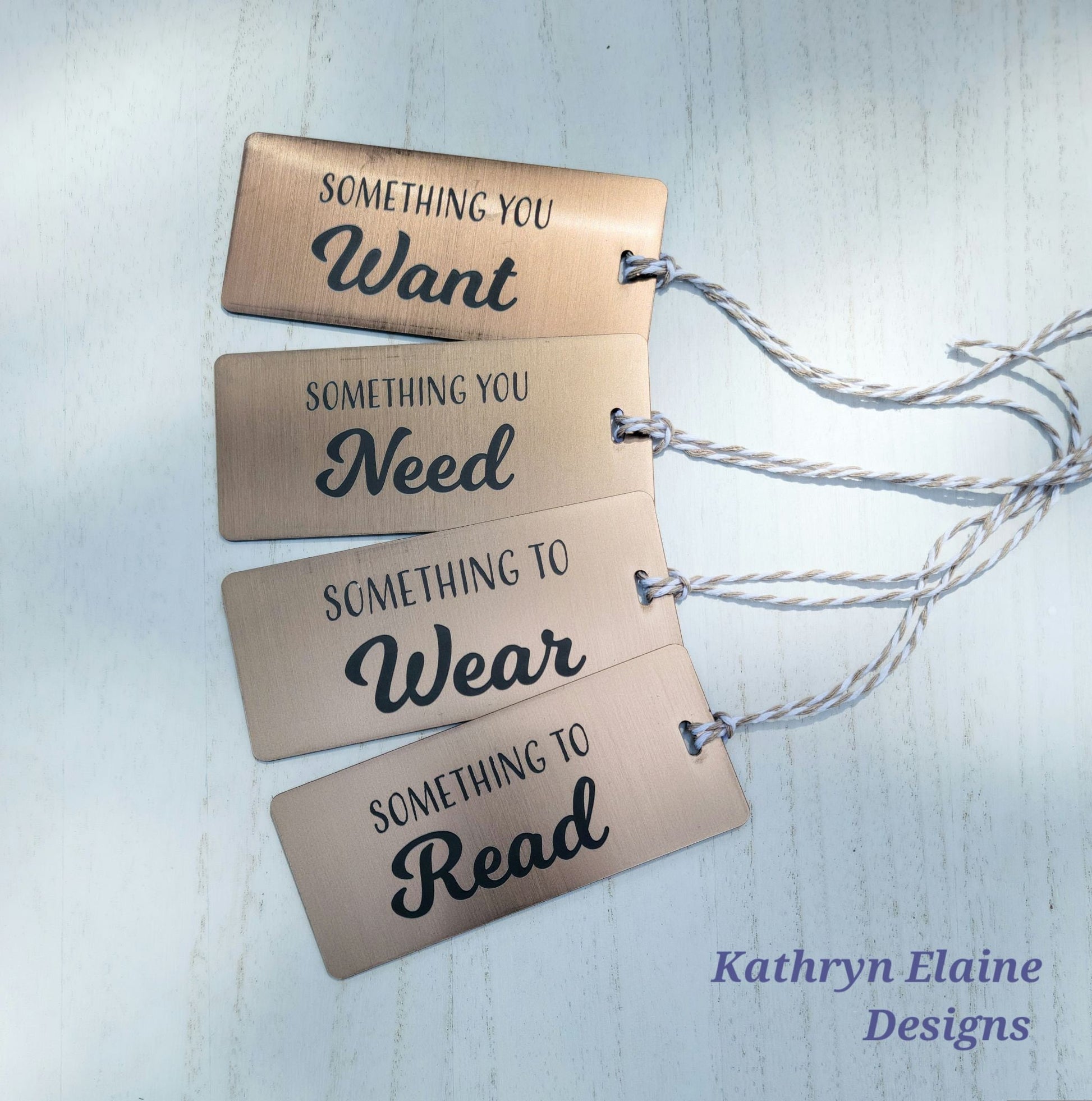 4 gift tags in bronze with gray lettering reading something you want, something you need, something to wear, something to read on white background