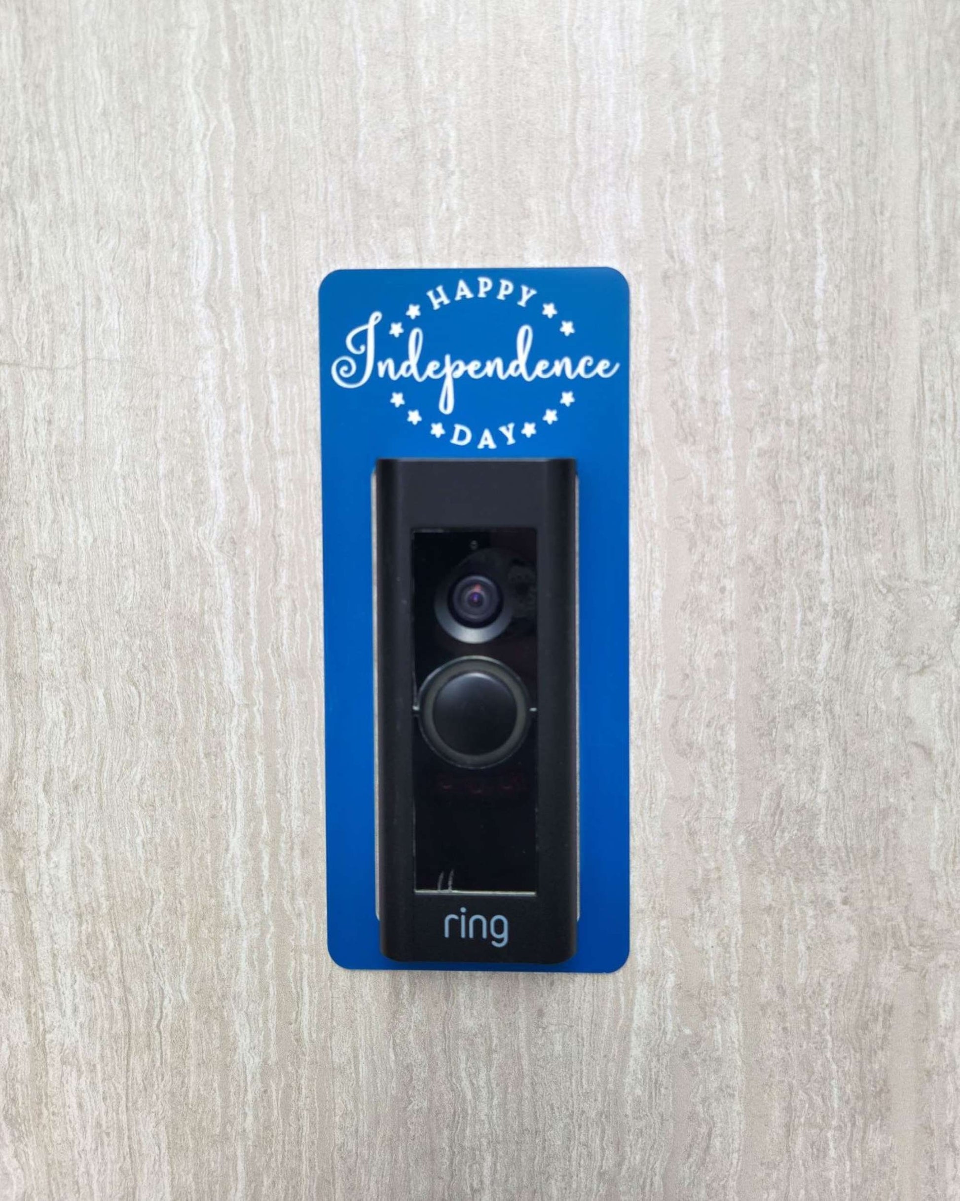 Blue laminate doorbell surround with white lettering saying Happy Independence Day and stars on ring doorbell and gray background