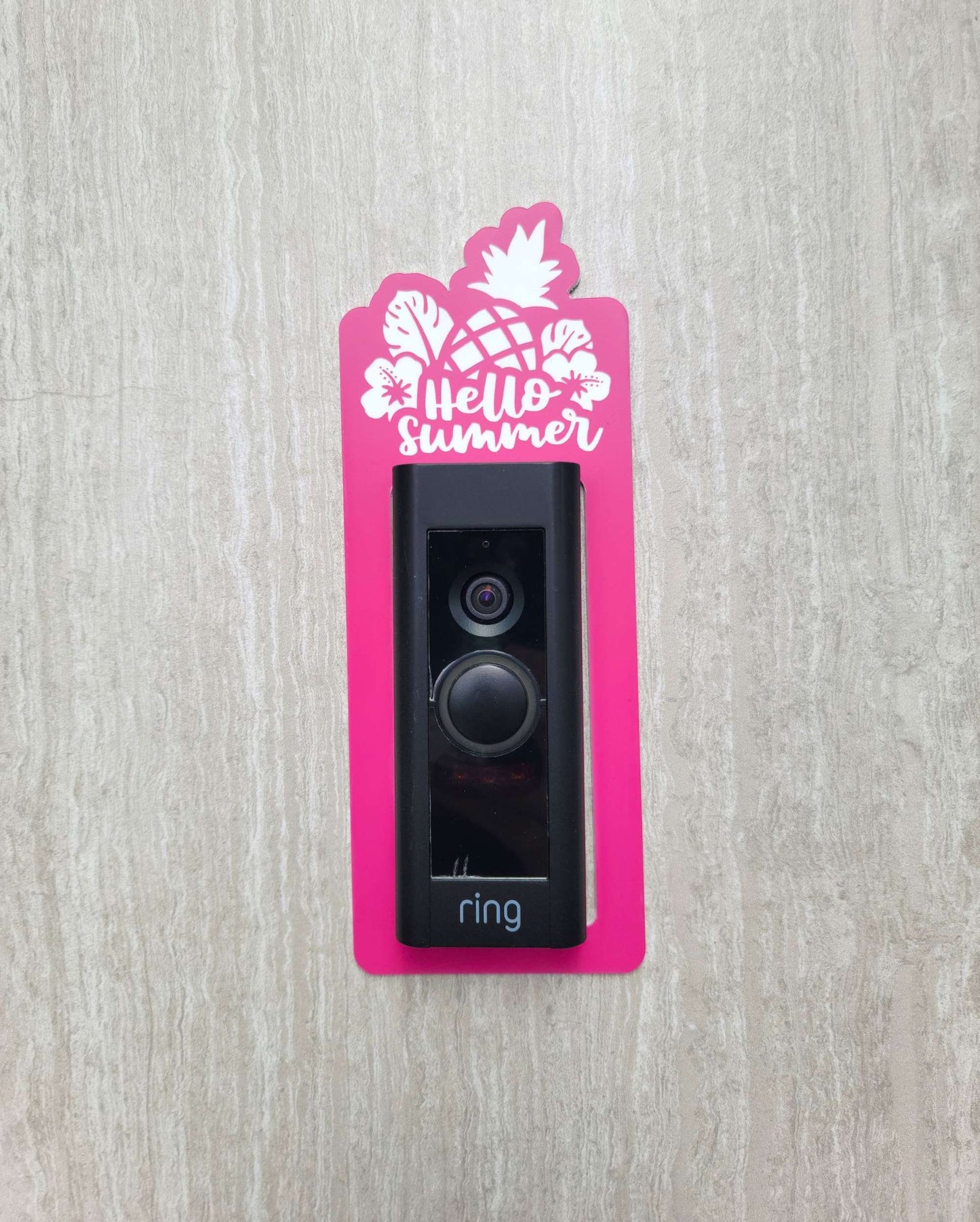 Pink laminate doorbell surround with white pineapple, leaves, and flowers and lettering saying hello summer on ring doorbell and gray background